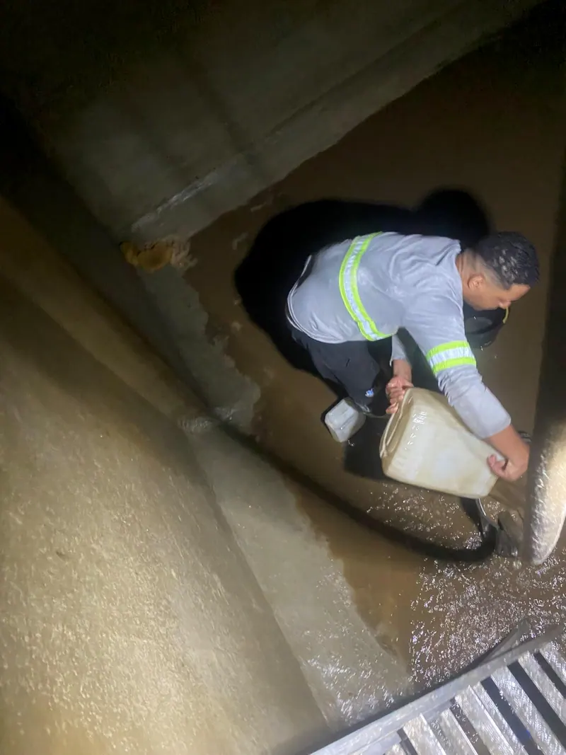 Funcionário de uniforme no canto da cisterna de concreto tirando com balde a água que sobrou
