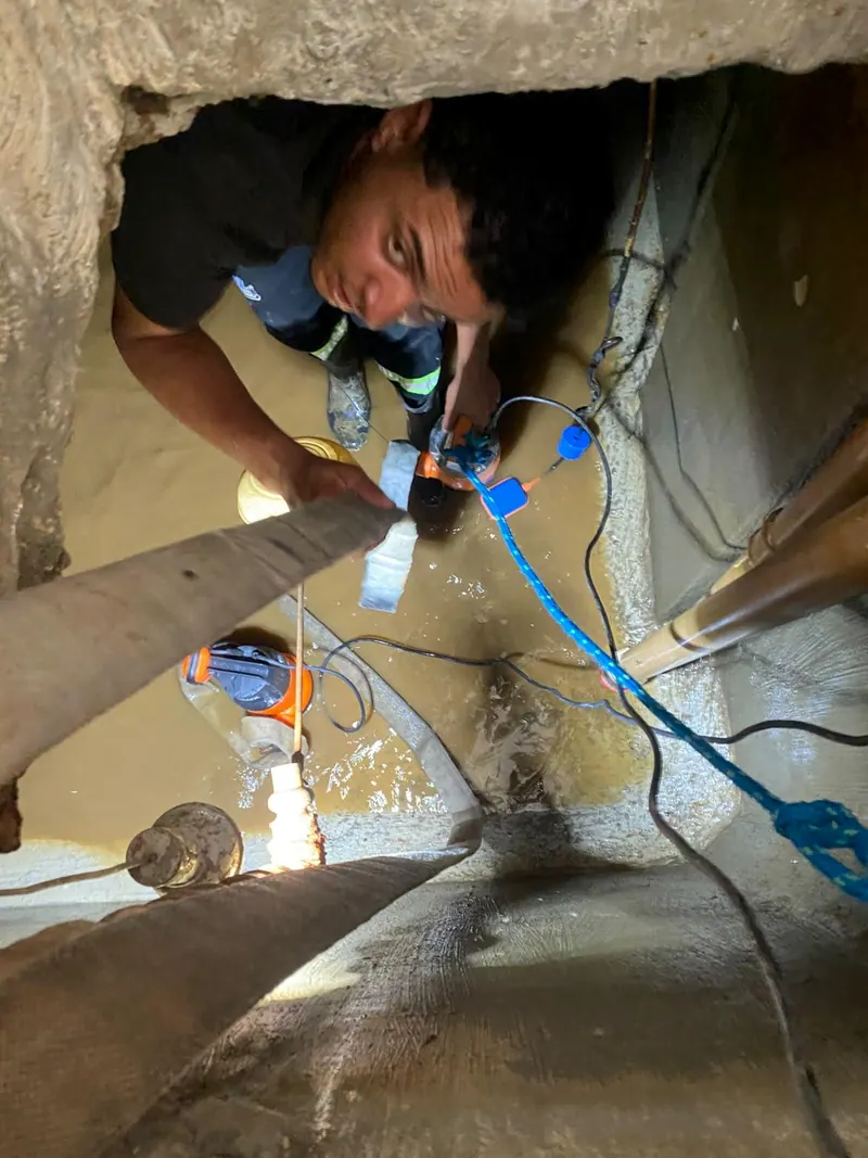 Funcionário passando pela abertura da cisterna, com a mangueira da bomba